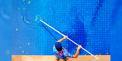 Young adult man personnel cleaning the pool from leaves.