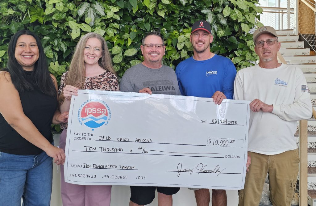 A group holds a large check for $10,000 made out to Child Crisis Arizona, surrounded by lush greenery indoors.