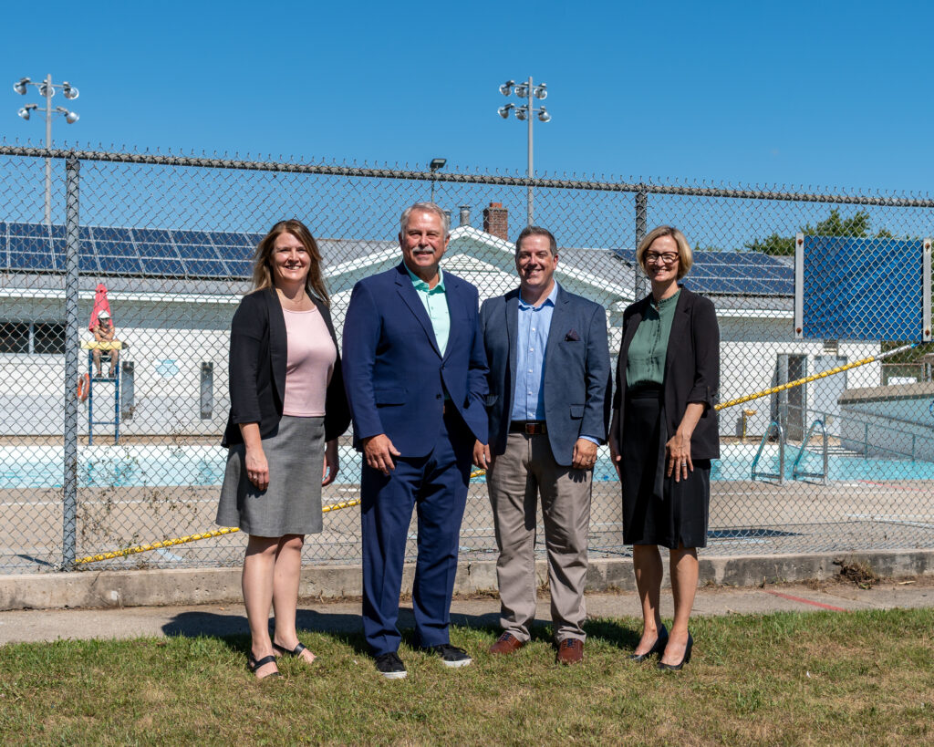 Four professionals stand together in front of a pool with solar panels, under a clear blue sky, creating a collaborative atmosphere.