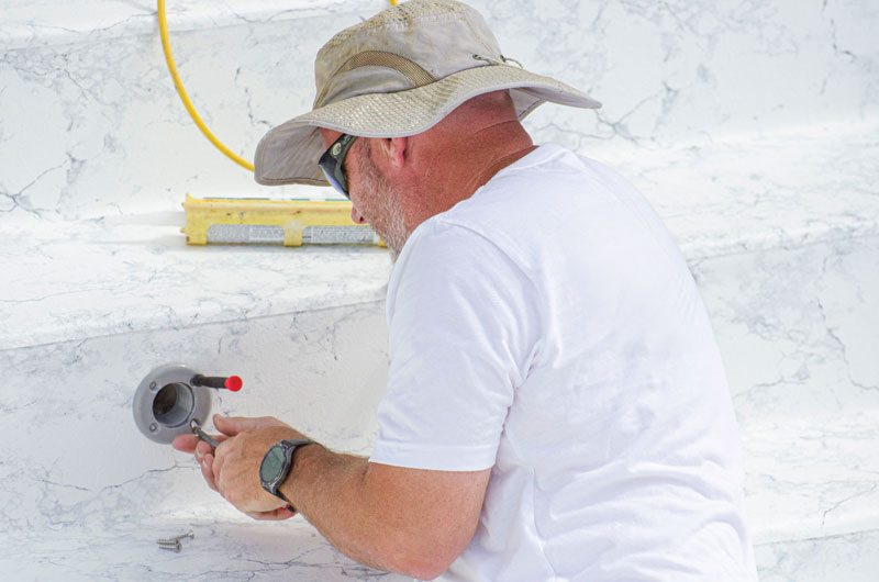 A person in a white shirt and beige hat is installing a fixture on a marble-patterned surface using tools.
