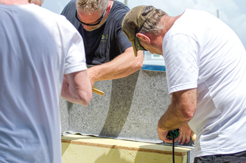 Two individuals work collaboratively on a construction project, handling materials and tools under a sunny sky.