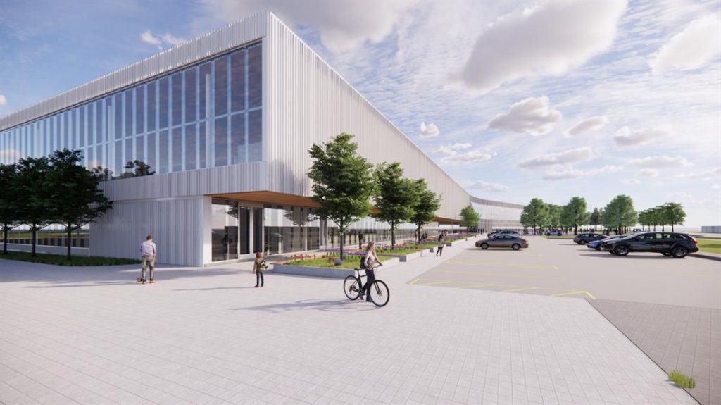 Modern commercial building with glass windows, trees, people walking and biking, and a parking lot under a partly cloudy sky.