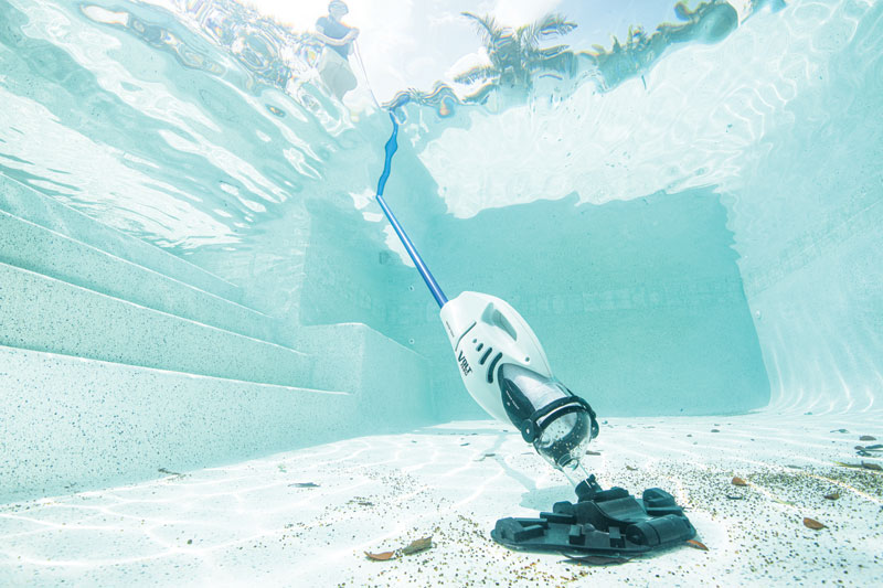 Underwater view of a pool with steps, featuring a robotic pool cleaner on the bottom. The water is clear, reflecting leafy patterns from above.