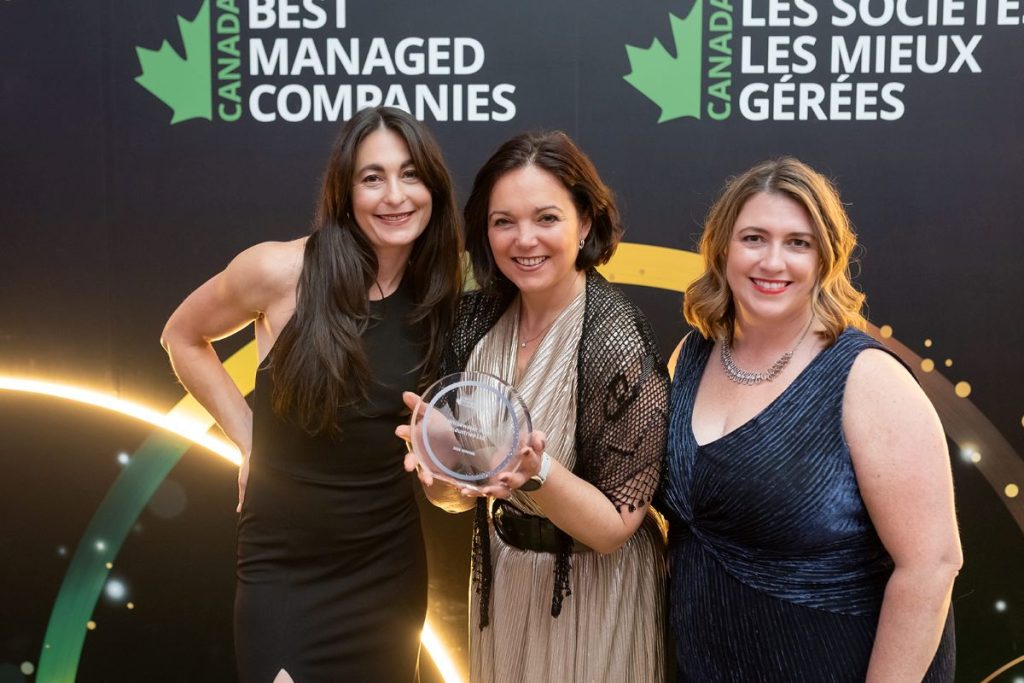 Three women smiling and posing with an award at the Canada’s Best Managed Companies event. They stand in front of a branded backdrop.