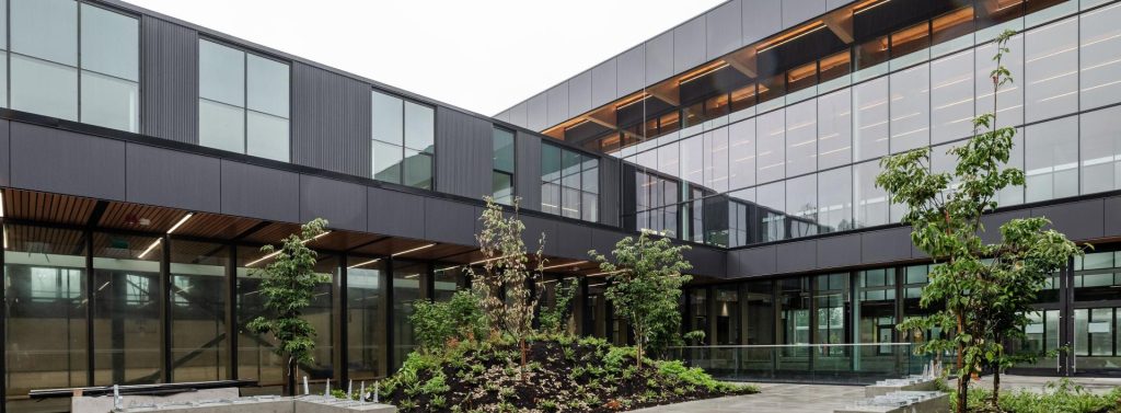 Modern architectural building with large glass panels and a courtyard filled with plants and small trees.
