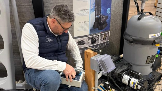 Man kneels beside pool equipment and tools while working on a control panel in a retail showroom.