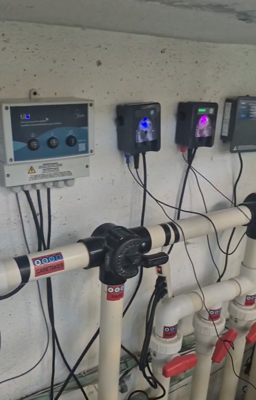 Industrial PVC piping with red-handled valves, warning labels, cables, and wall-mounted electrical control boxes.
