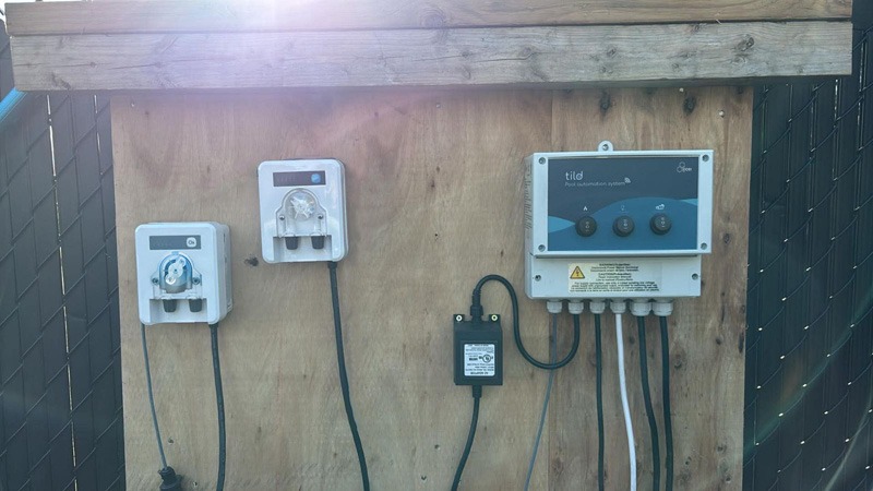 Wooden panel with multiple wired electrical controls, including a large blue-and-white “tilo” control box on the right.