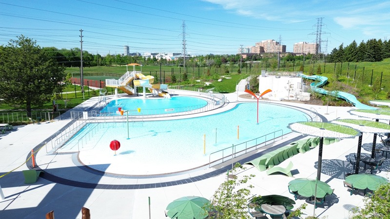 Outdoor aquatic center with turquoise pools, colorful water features, slides, lounge chairs, and shade umbrellas.