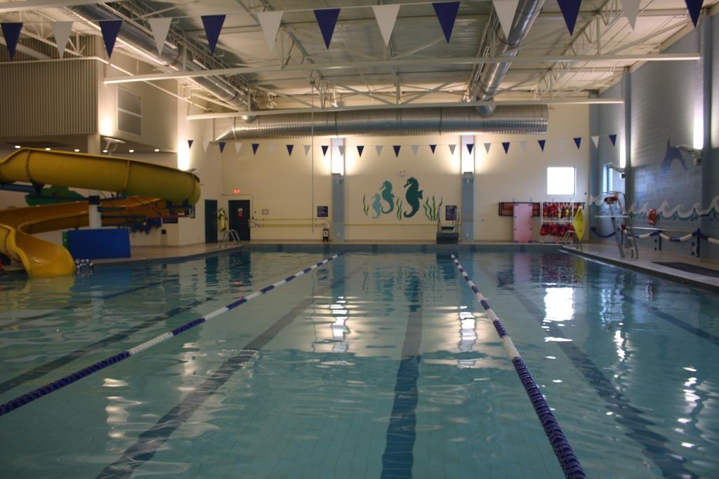 Indoor swimming pool with lap lanes, a yellow waterslide, blue-and-white pennants, and an aquatic mural.