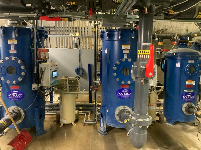 Filtration technology Industrial mechanical room with three large blue ACAPULCO-labeled tanks, overhead piping, valves, and control equipment.