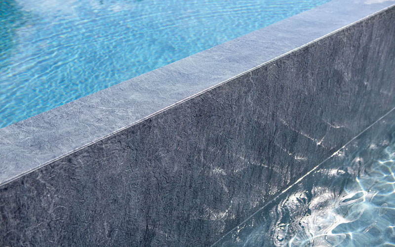 Close-up of rippling turquoise pool water beside a dark gray stone pool edge and wall.