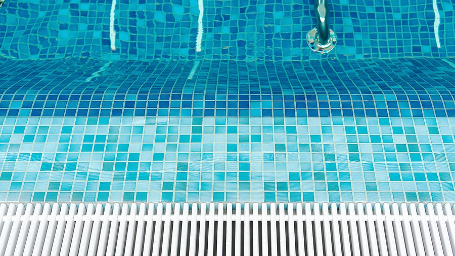 Close-up of a blue-tiled swimming pool with a metal wall fixture and white drainage grate.
