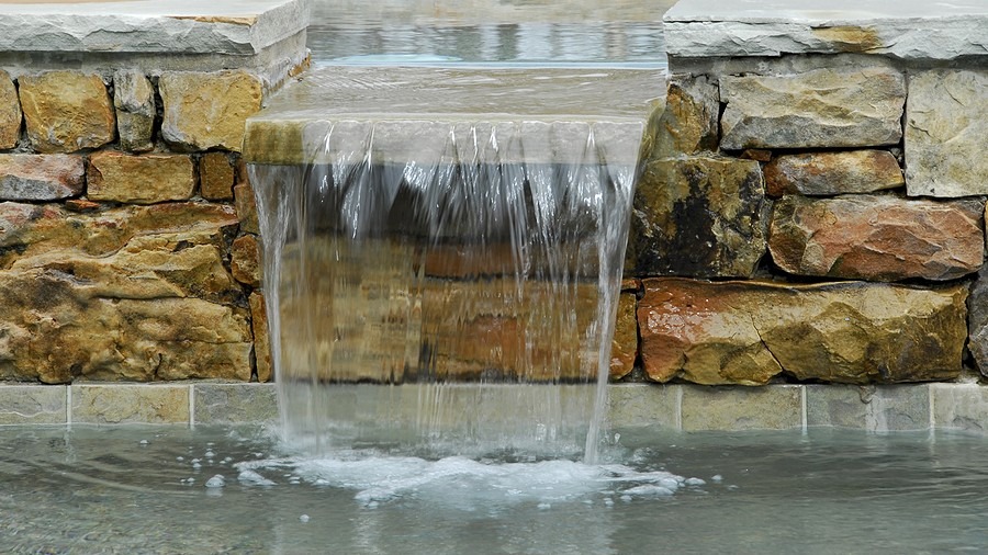 Water cascading over a stone ledge into a shallow pool.