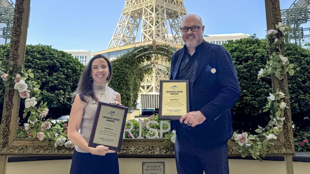 Two people pose with Leading Edge Awards in front of a flower-covered frame and an Eiffel Tower–style structure.